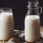 Oat milk in two jars on a table with a cloth and oats
