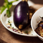 Roasted eggplant served in a bowl with a full eggplant on a plate in the background