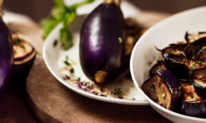 Roasted eggplant served in a bowl with a full eggplant on a plate in the background
