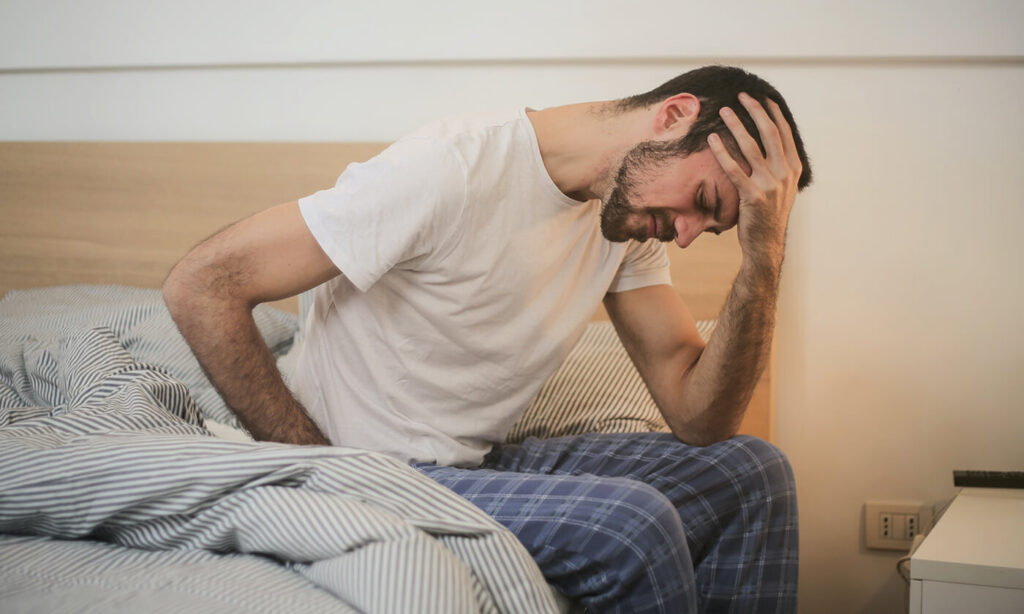 Person hungover sitting on the edge of a bed holding his head