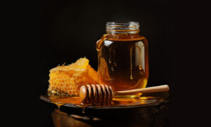 Honey dripping from a jar with a piece of honeycomb and a wooden dipper